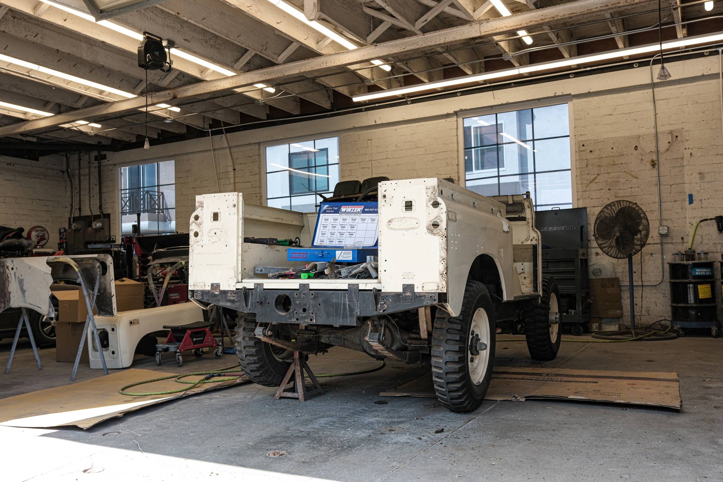 A vintage Land Rover stripped to its bare tub on stands in the body shop, loose body panels beside it.