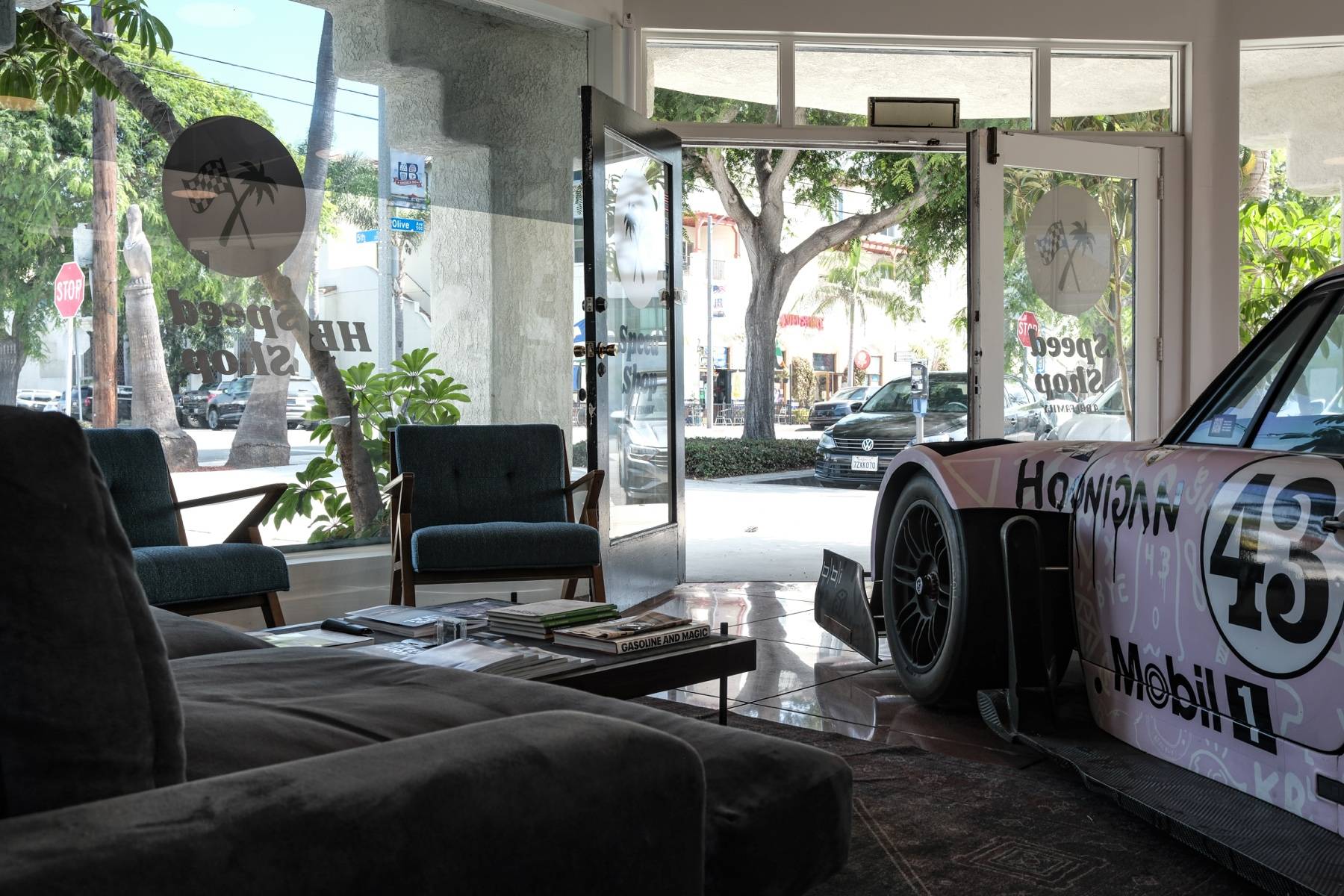 The front lounge: a sofa and armchairs facing glass doors that open onto 5th Street, the pink Hoonigan 911 parked inside.