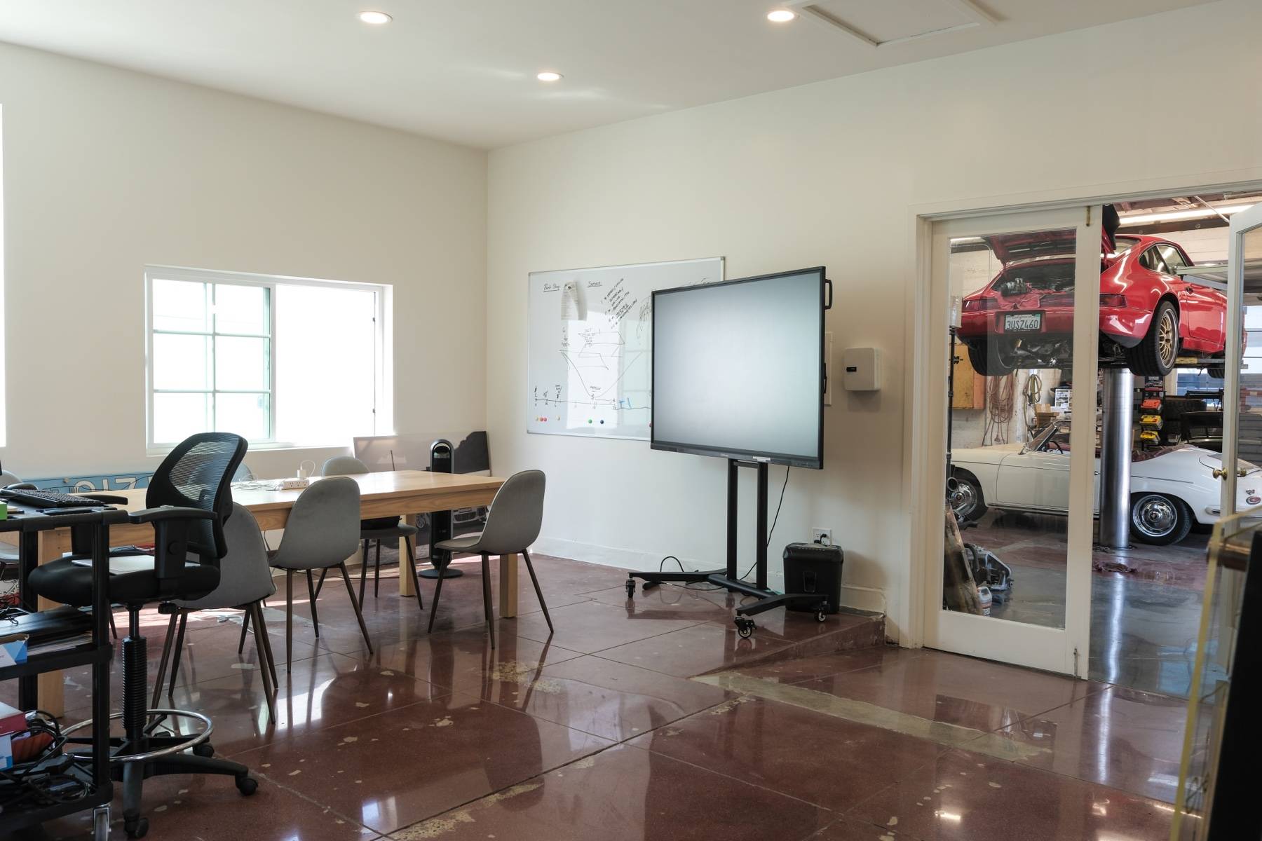 A room with a long table, a whiteboard, and a screen, with glass doors looking into the service bay.
